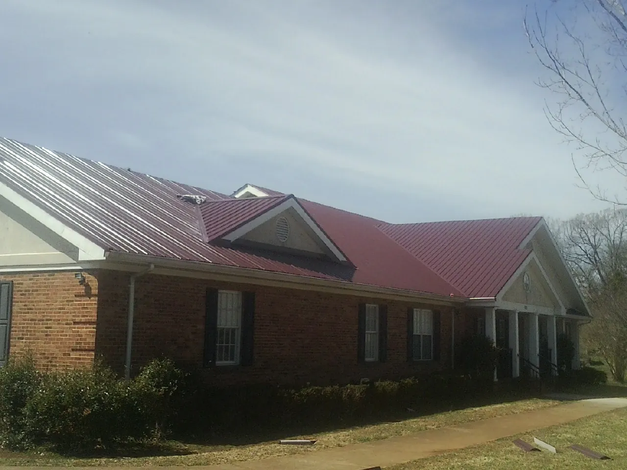 Red metal roof with gabled entries on a long brick building, from a Hail Damage Roof Repair job in Hooper