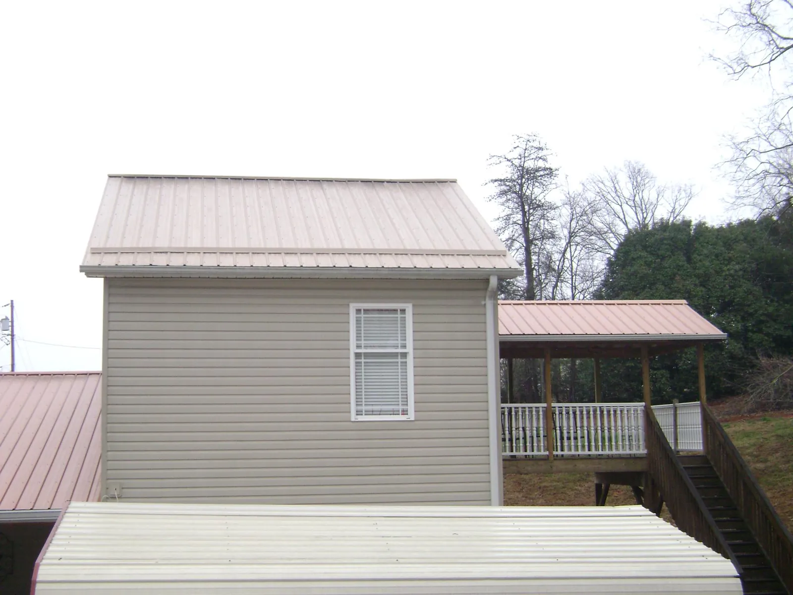 Tan metal roofs on a two story addition and attached porch, from a Roof Replacement job in Hooper